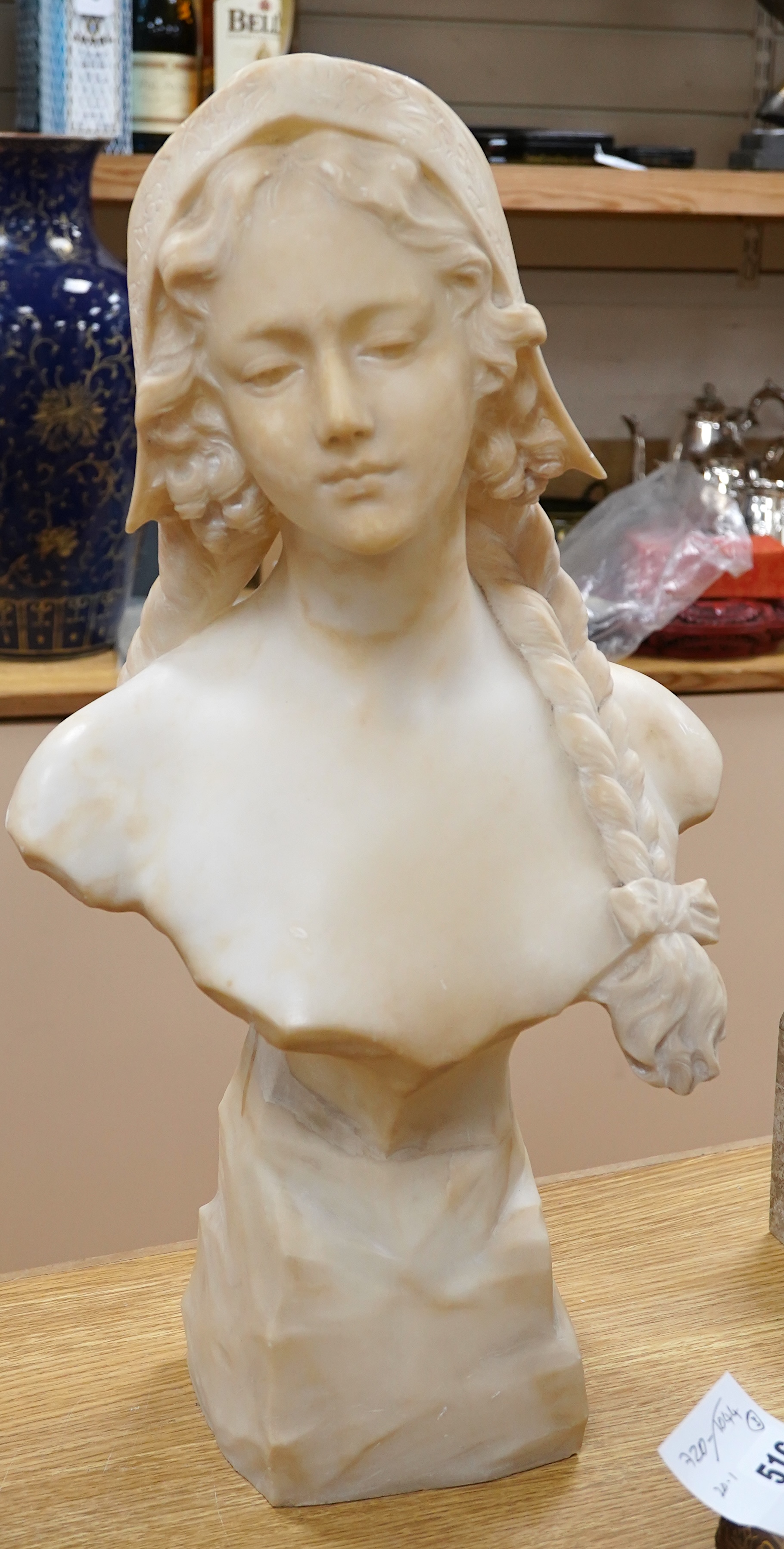 A French alabaster bust of a girl with long plait wearing a hat, signed on the back of pedestal, 54cm high. Condition - good